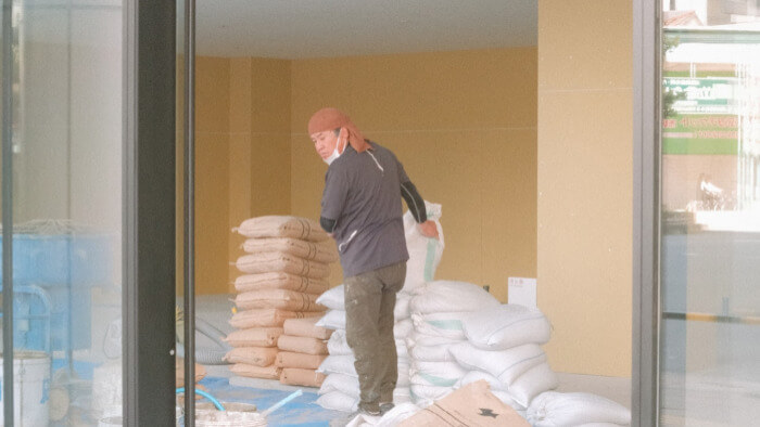 Flooring specialist of contractor hired for commercial renovation moving bags of cement pre-mix